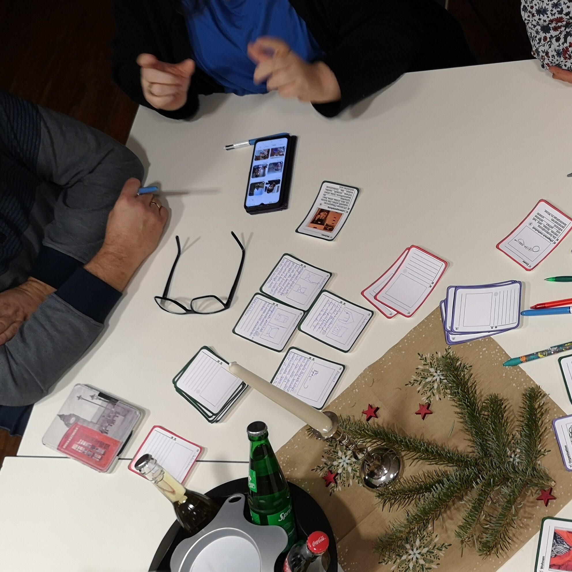 Tisch mit verschiedenen Spielkarten und Deko. Hände von Menschen, die am Tisch sitzen.